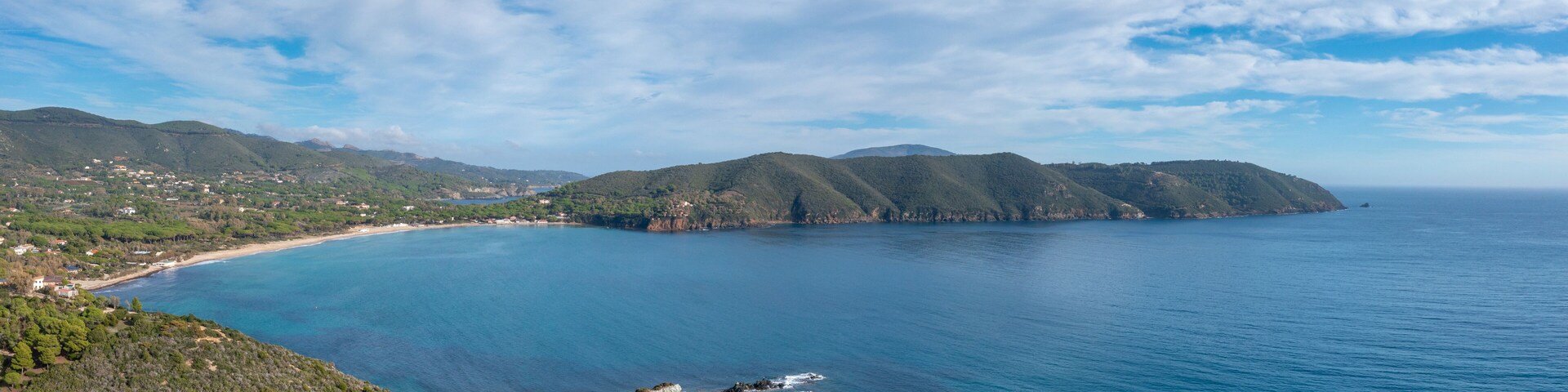 Un paisaje costero con mar azul transparente, playas de arena y colinas verdes.