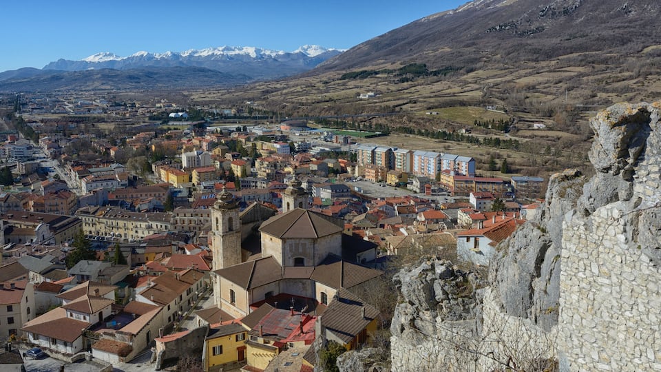 A town with historic buildings, a prominent church, and snow-capped mountains in the background.