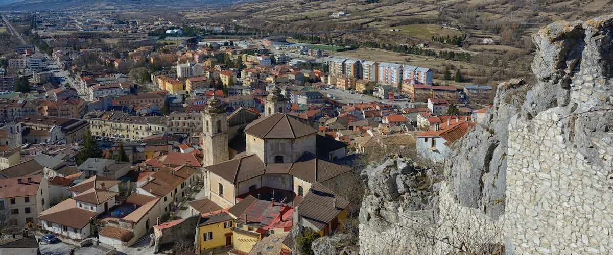 A town with historic buildings, a prominent church, and snow-capped mountains in the background.