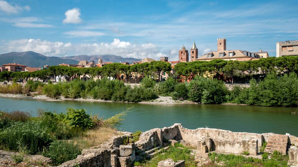 A river with ruins and buildings in the background.