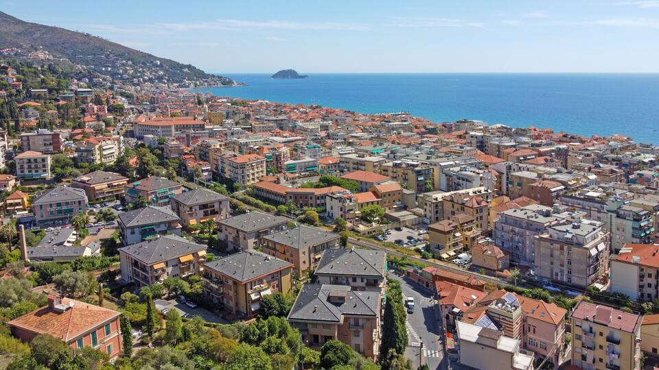 A coastal town with dense housing, a prominent hill in the background, and a small island in the sea.