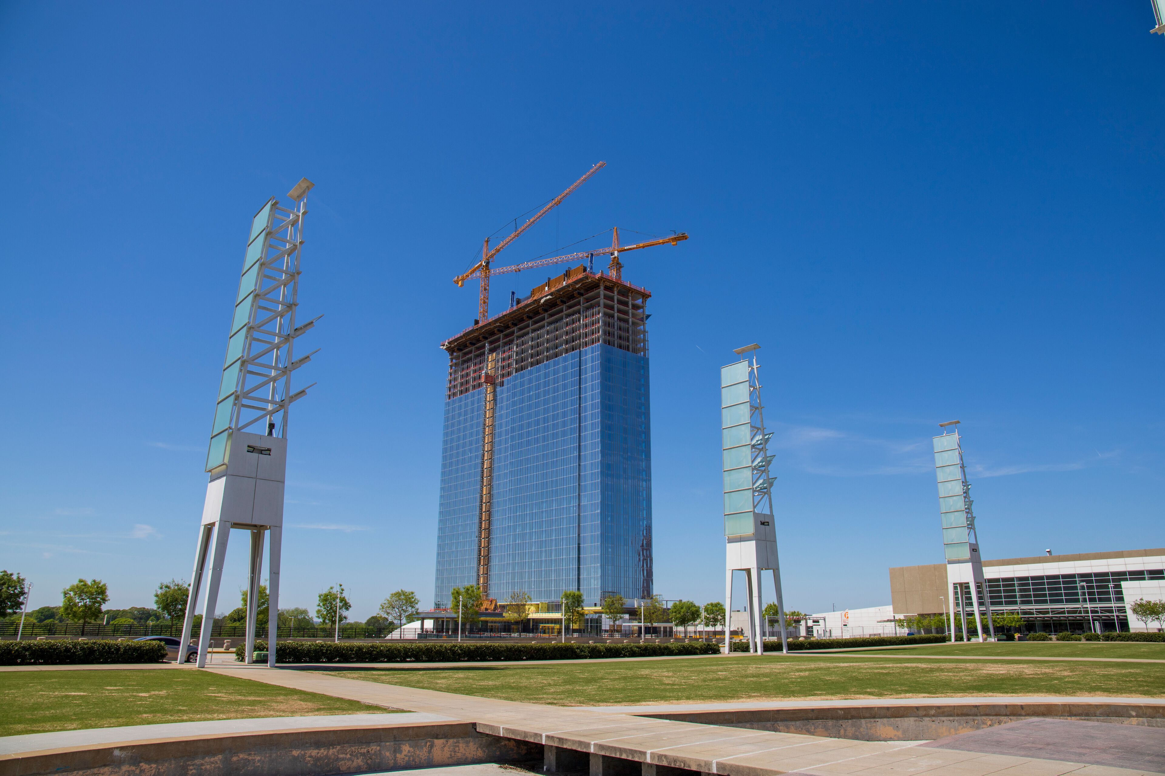 A gorgeous spring landscape at Georgia International Plaza with green trees and grass and a glass skyscraper under construction with tower cranes and a clear blue sky in Atlanta Georgia USA