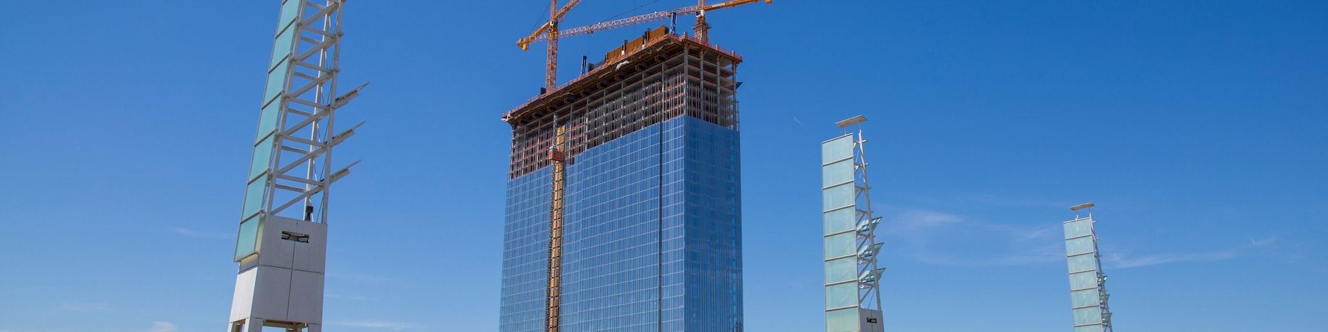 A gorgeous spring landscape at Georgia International Plaza with green trees and grass and a glass skyscraper under construction with tower cranes and a clear blue sky in Atlanta Georgia USA