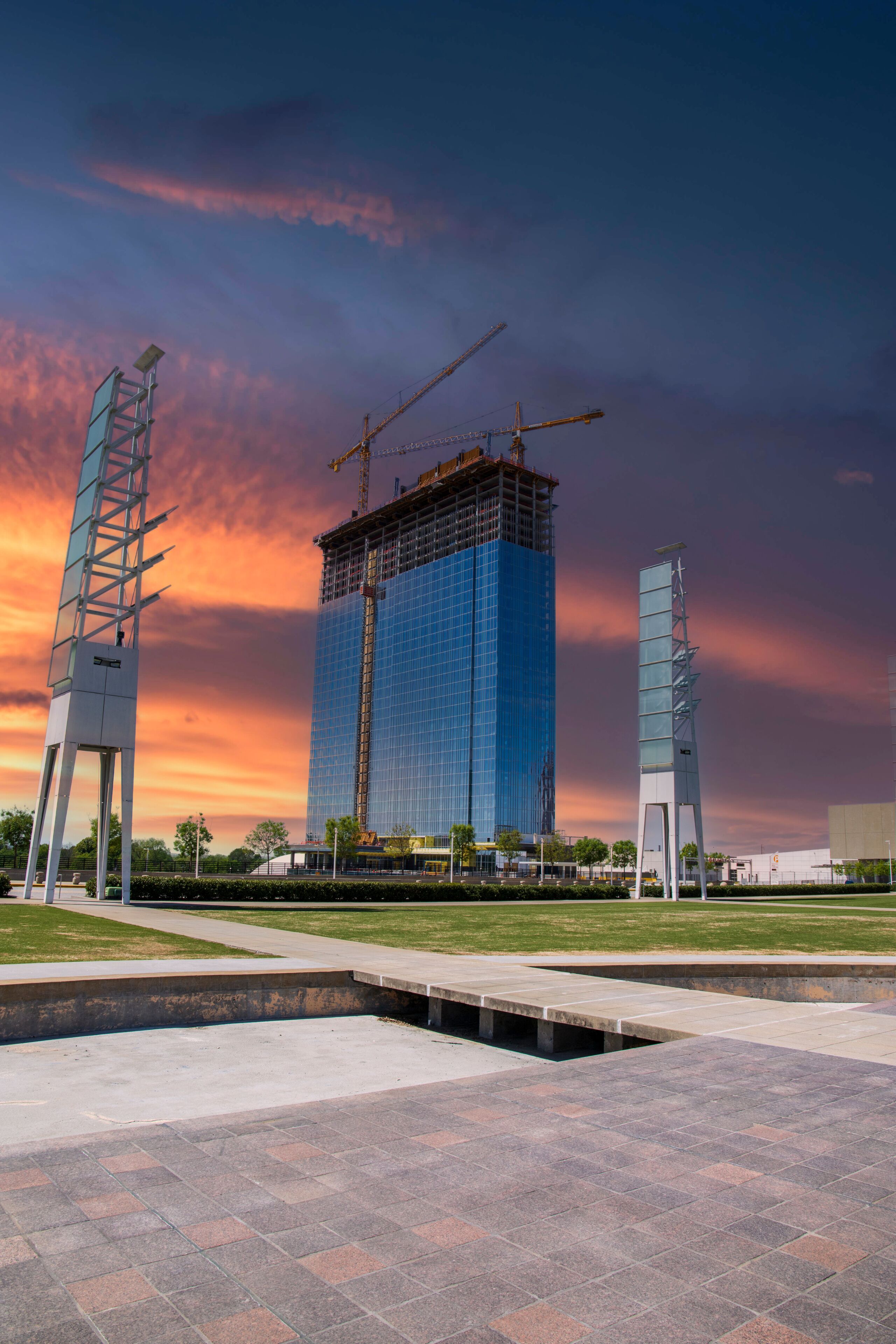 A gorgeous spring landscape at Georgia International Plaza with green trees and grass and a glass skyscraper under construction with tower cranes and powerful clouds at sunset in Atlanta Georgia USA
