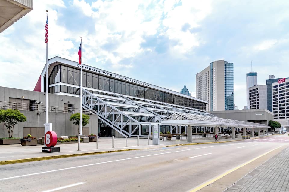 The Georgia World Congress Center with a modern glass facade, a large 'B' sign, and surrounding urban buildings.