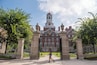 A historic building with a clock tower, a large gate, and a well-maintained lawn.