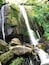 A waterfall cascading over large rocks surrounded by lush greenery.
