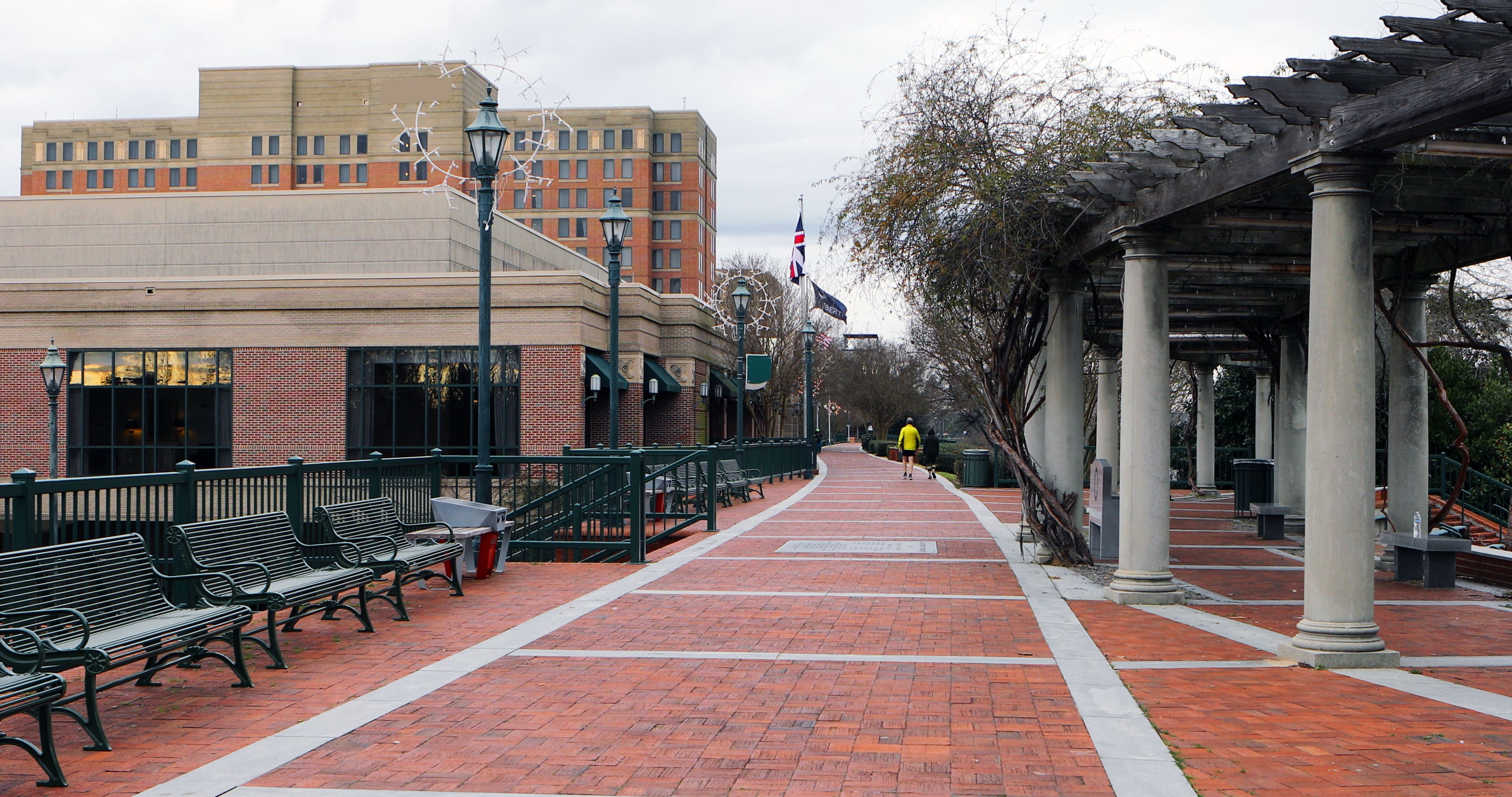 A brick-paved walkway with benches, a lamp post, and a building with a brick facade.