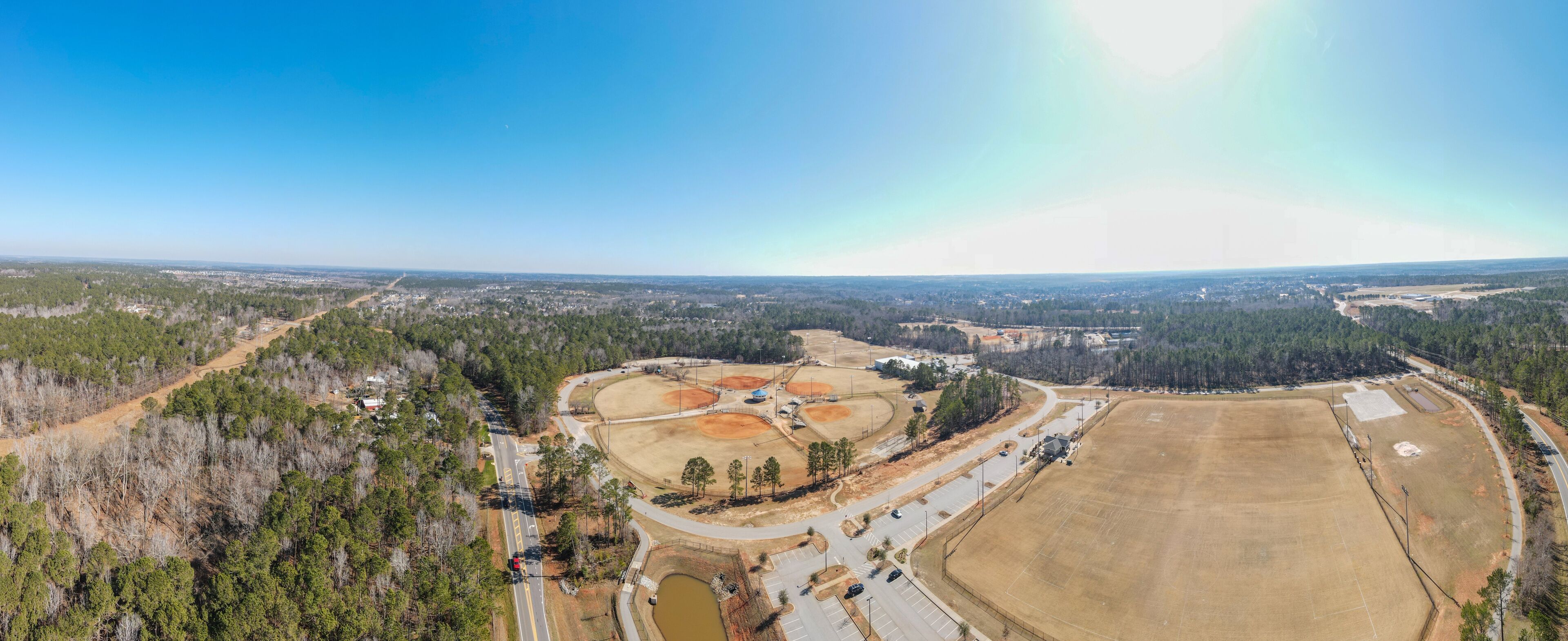 An aerial view of a baseball field surrounded by trees and a road.