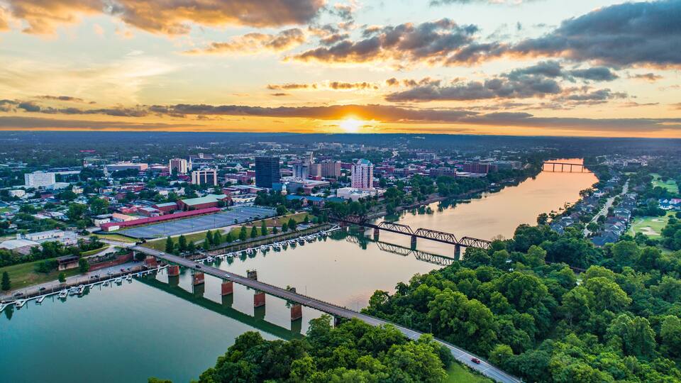 A cityscape with a river, a bridge, and a sunset.
