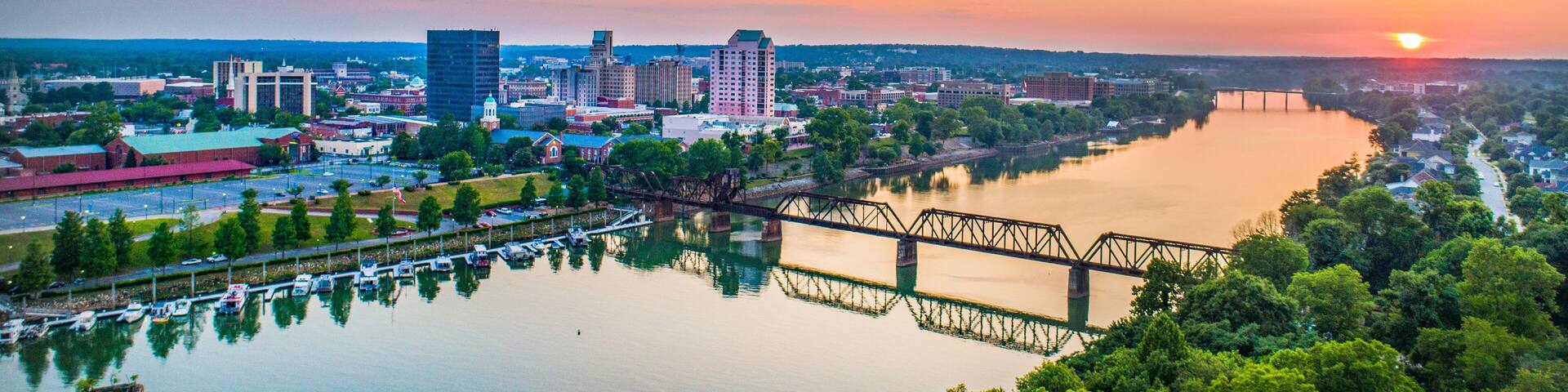 A cityscape at sunset with a river, a bridge, and various buildings.