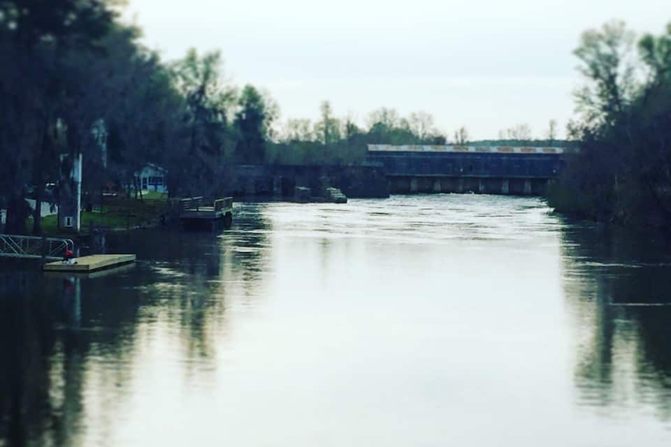Een rustige rivier met een brug op de achtergrond en een steiger aan de linkerkant.