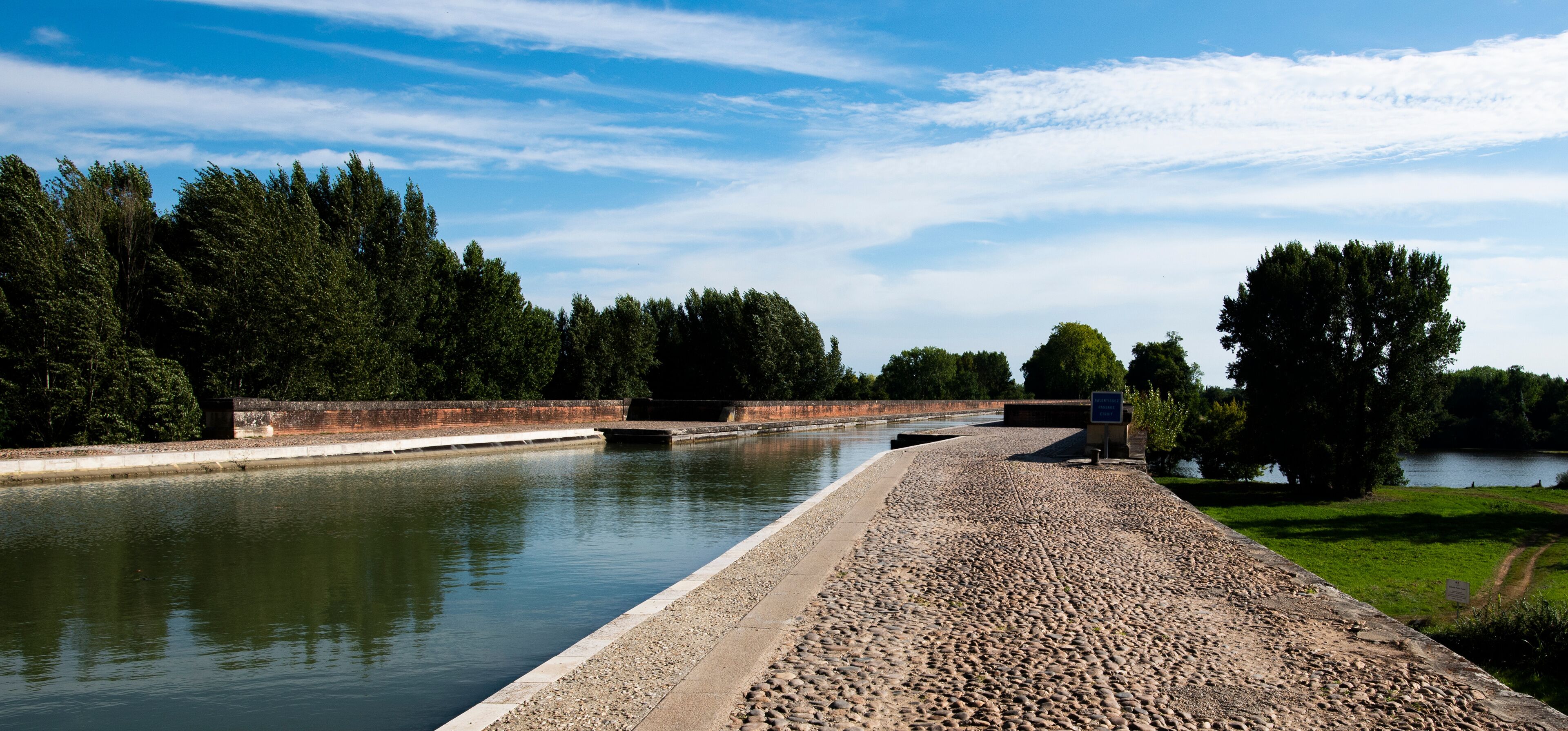 A canal with a paved walkway, trees, and a clear sky.