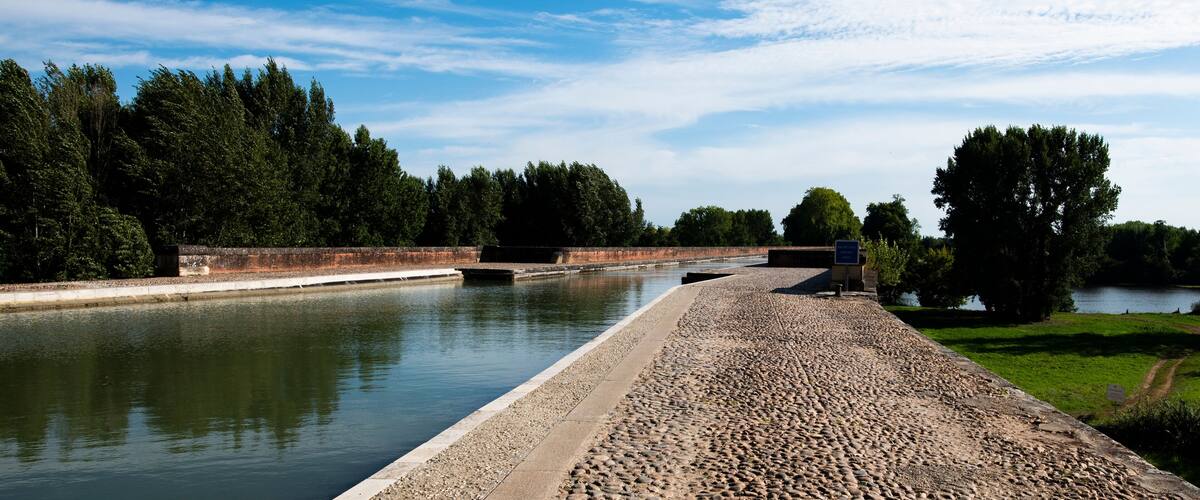 A canal with a paved walkway, trees, and a clear sky.