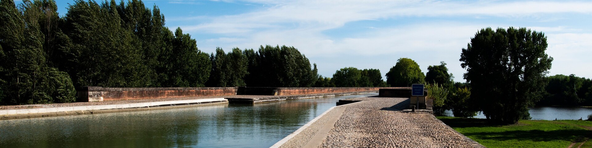 A canal with a paved walkway, trees, and a clear sky.