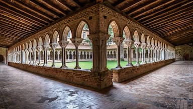 A cloister with a series of arches and columns, a brick floor, and a wooden ceiling.