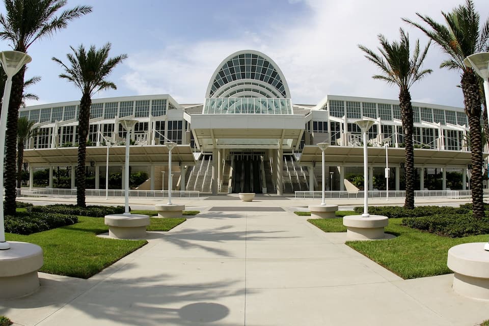 A modern building with a large arched entrance, surrounded by palm trees and a central pathway.