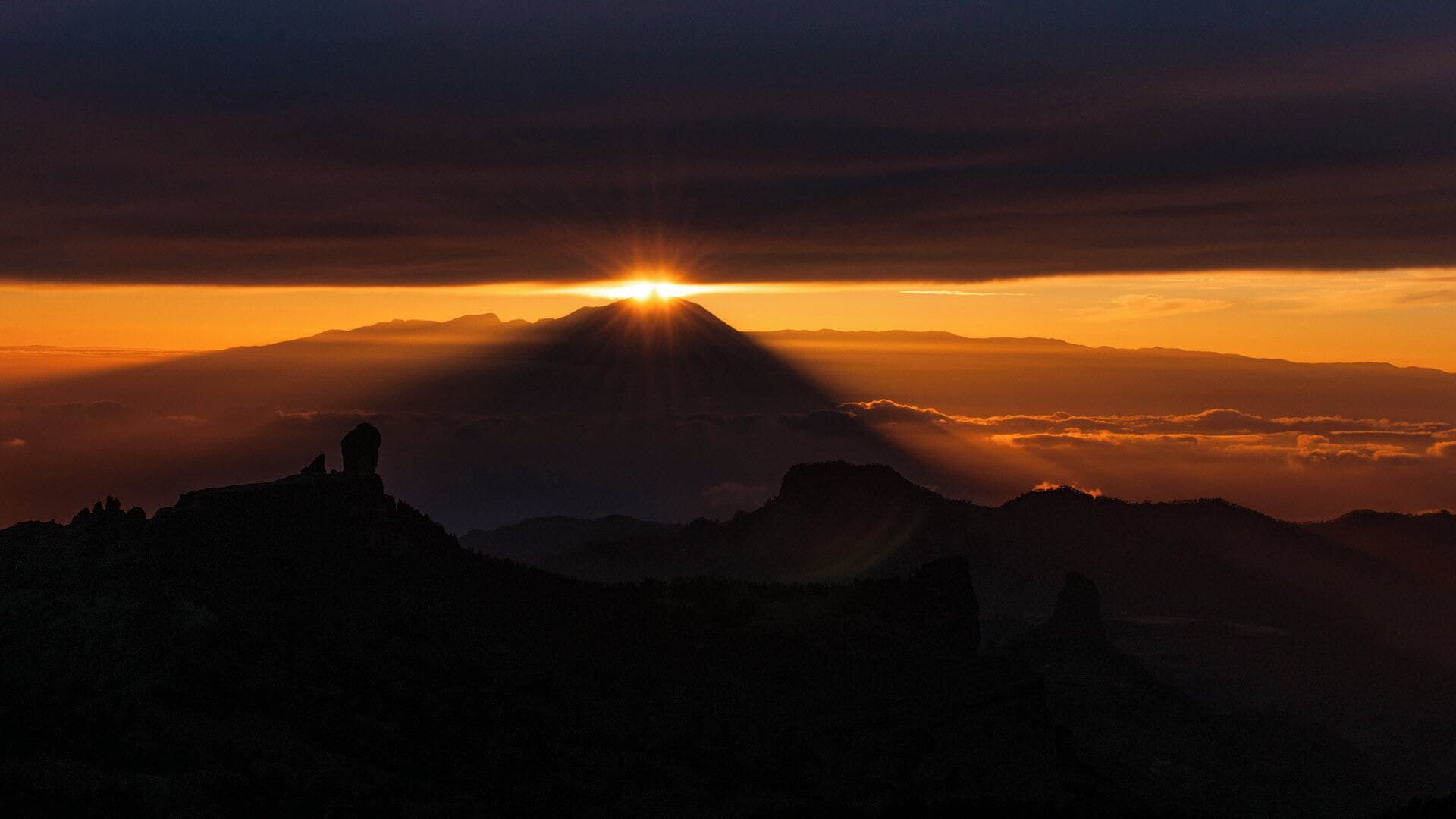 A mountain range with a sun setting behind it.