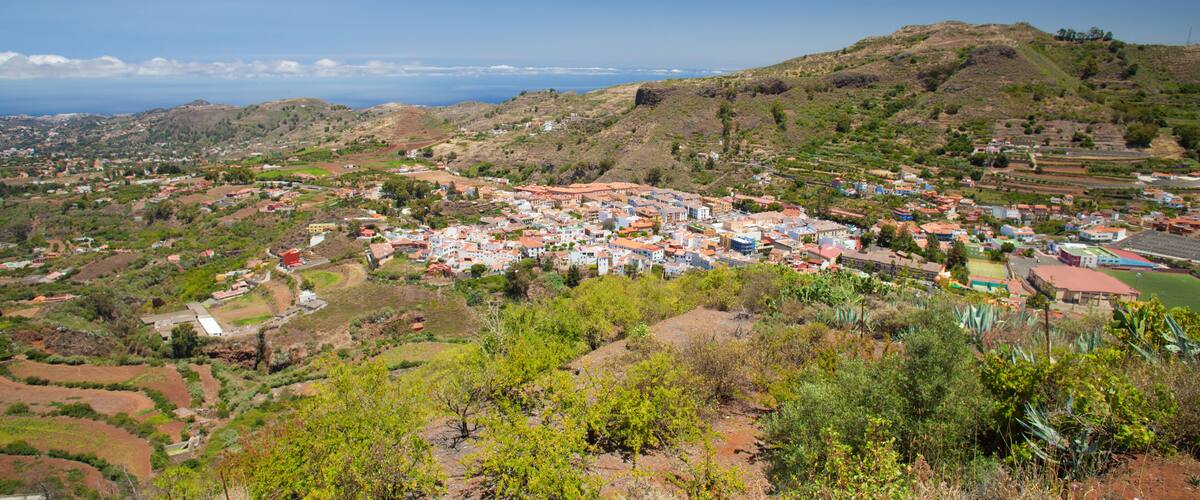 A coastal town with terraced fields, a hilltop church, and a clear view of the ocean.