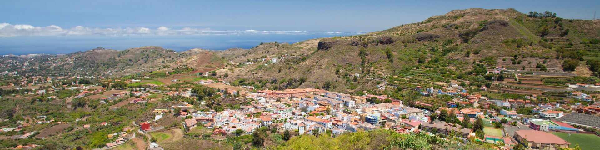 A coastal town with terraced fields, a hilltop church, and a clear view of the ocean.