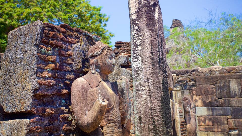 An ancient stone statue with a detailed headdress, set against a backdrop of weathered stone walls and a tree trunk.