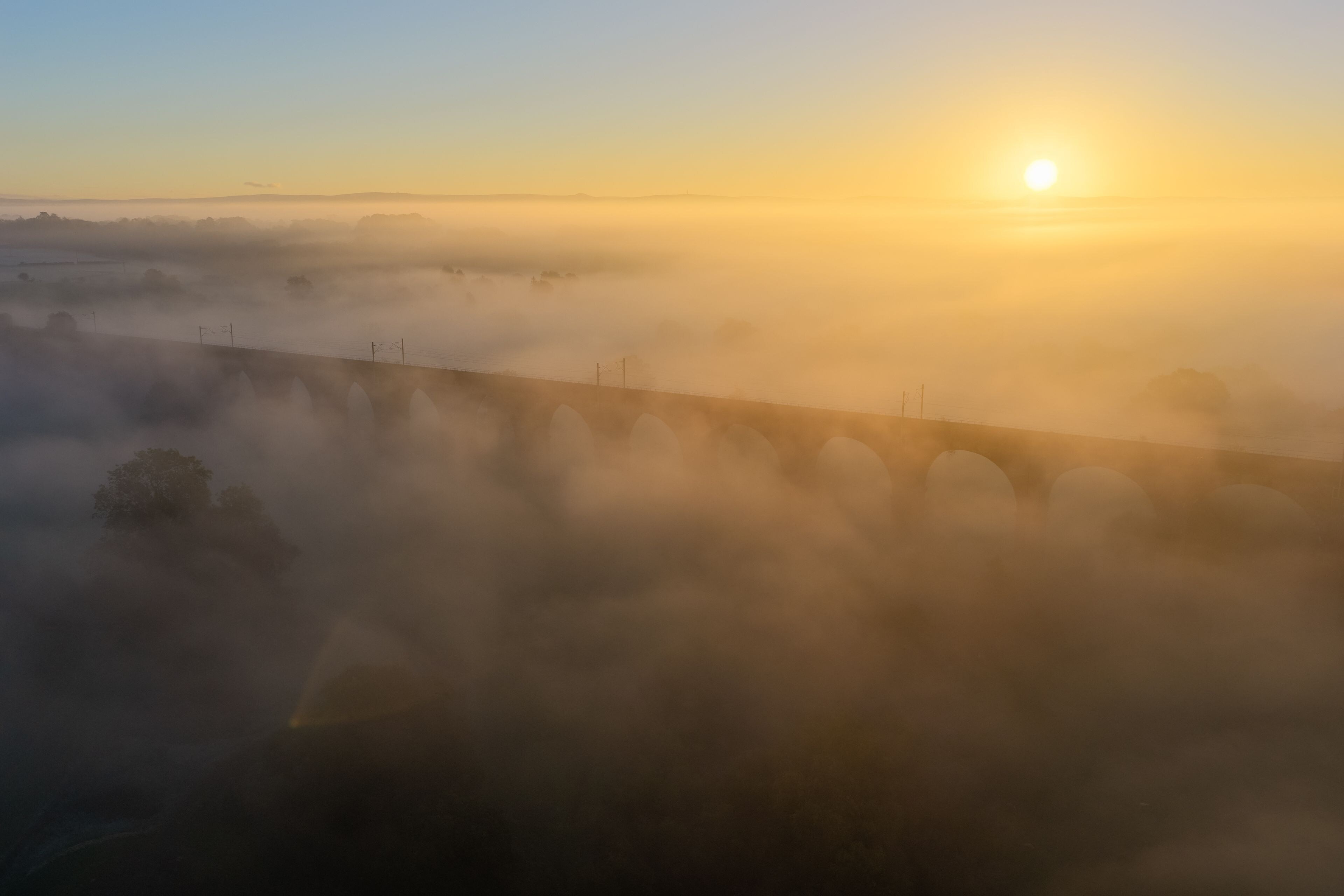 A sunrise over a fog-covered landscape with a bridge in the foreground.