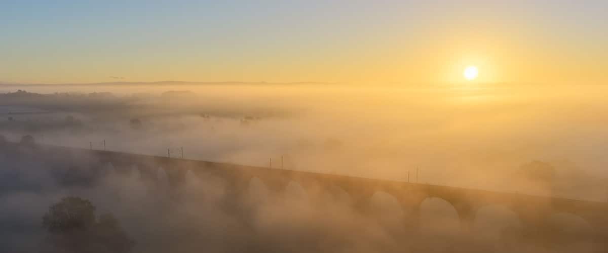 Amanecer sobre un paisaje cubierto de niebla, con un puente en primer plano.
