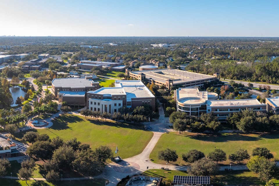 An aerial view of a university campus with multiple buildings, green spaces, and a lake.