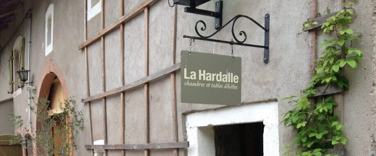 A rustic building with a sign reading "La Hardalle chambres et tables d'hôtes" and a wooden gate in front.