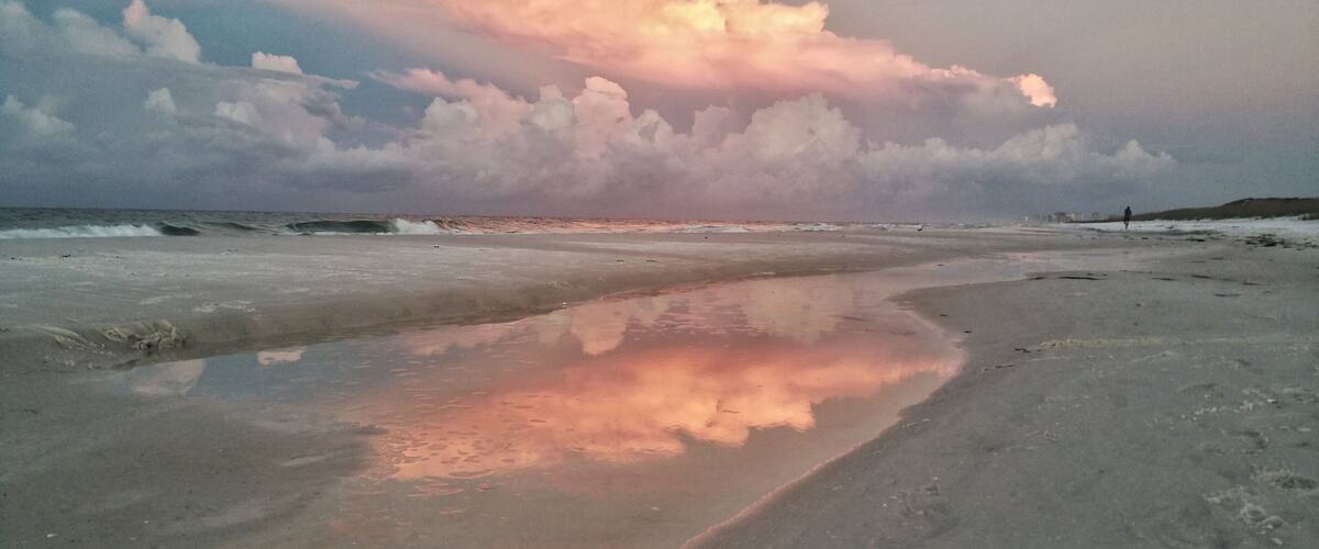 A beach with a reflective puddle, waves, and a cloudy sky.