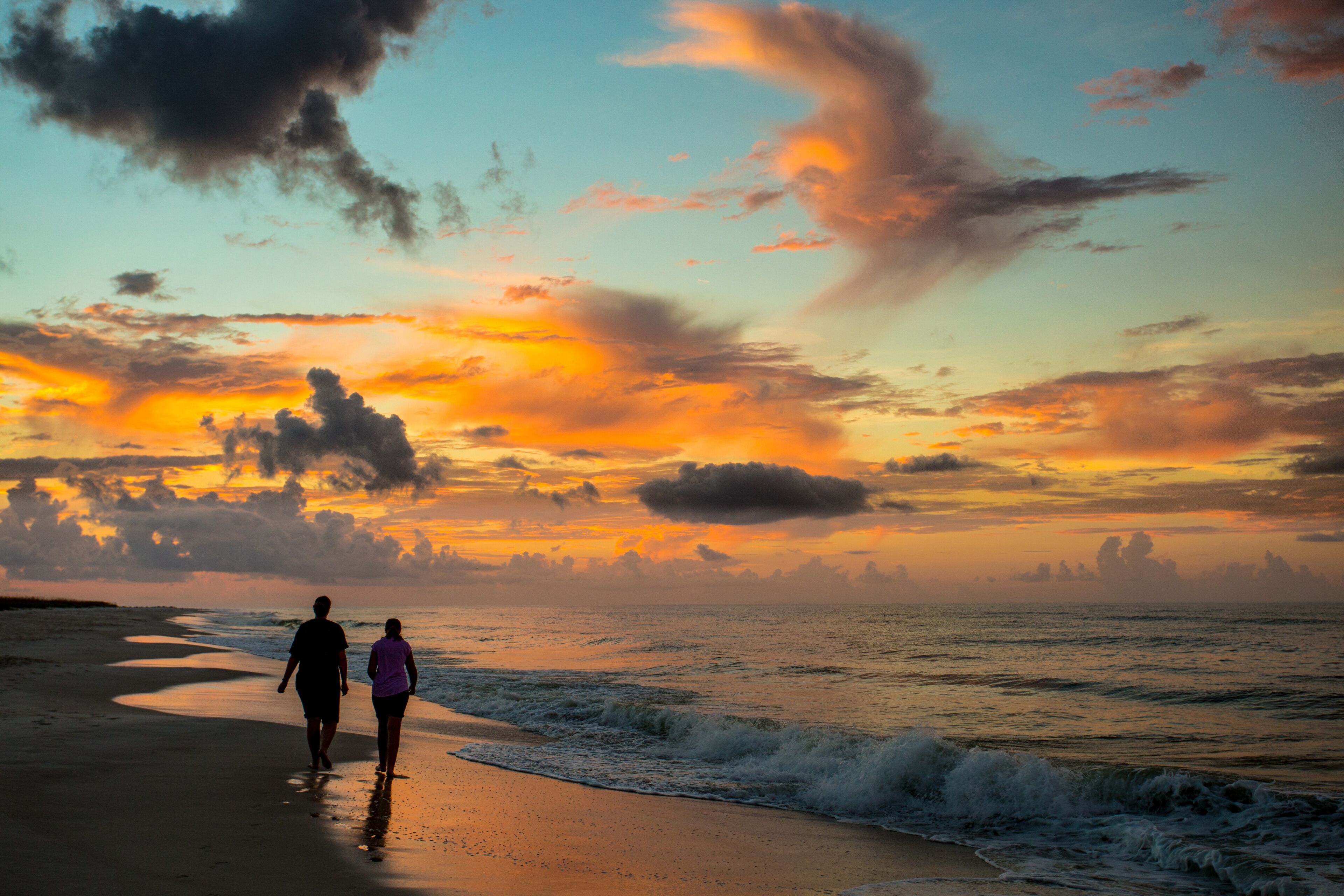 A sunset over a beach with two people walking along the shore.