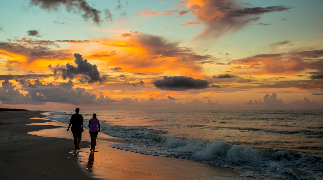 A sunset over a beach with two people walking along the shore.
