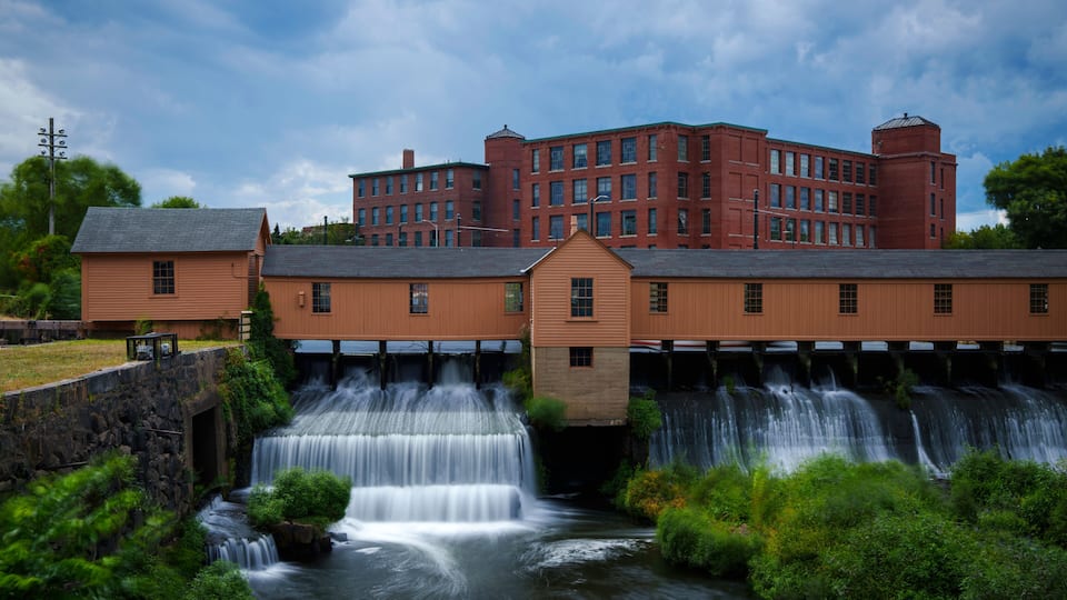 A waterfall cascading over a wooden structure with a red brick building in the background.