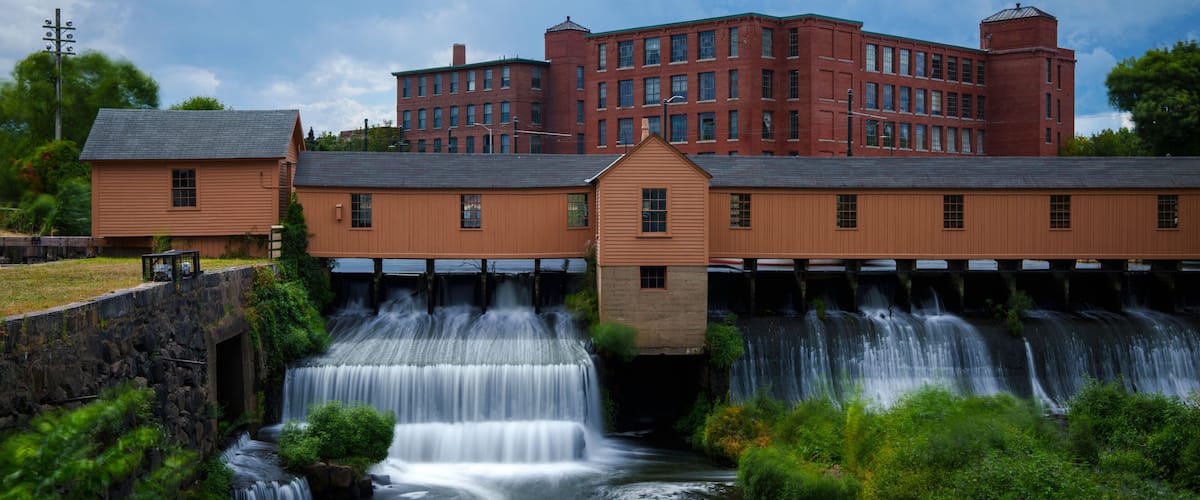 A waterfall cascading over a wooden structure with a red brick building in the background.