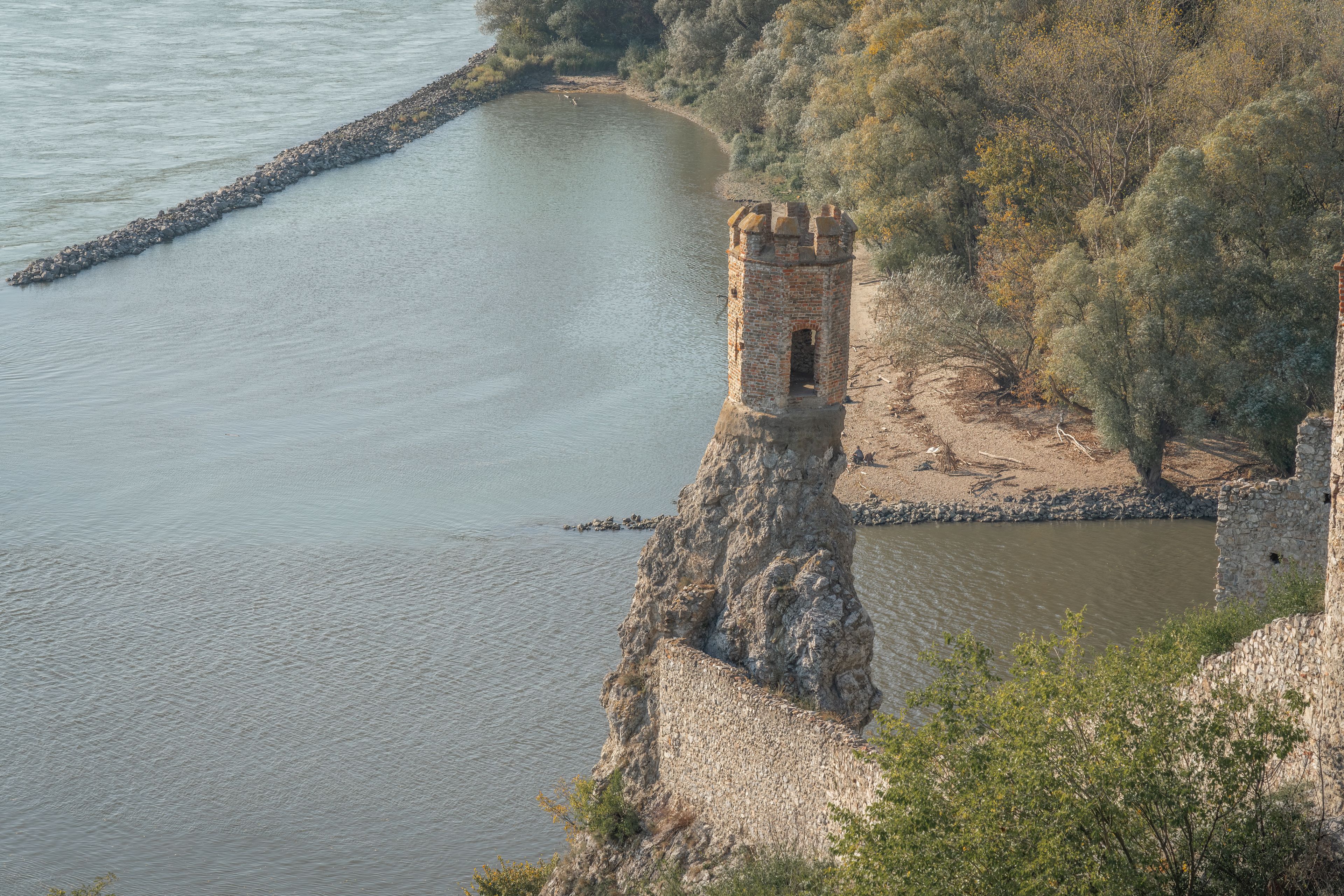 Un río con un puente de piedra y una torre en una colina.