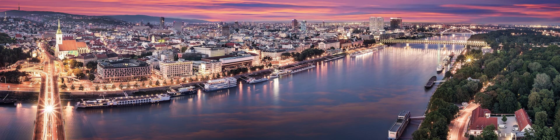 A cityscape at dusk with a river, a prominent church, and a bridge.