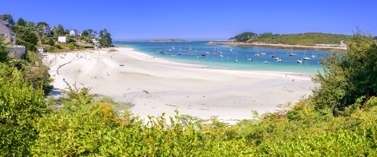 A beach with white sand, clear turquoise water, and several boats anchored near the shore.