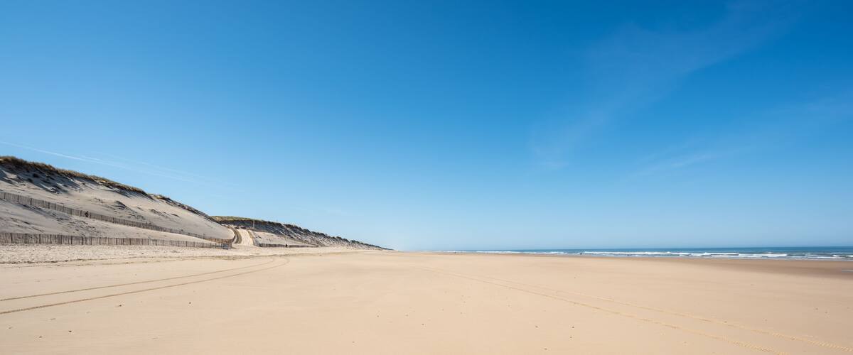 A sandy beach with a gentle slope leading to the ocean, clear skies, and a few distant people.