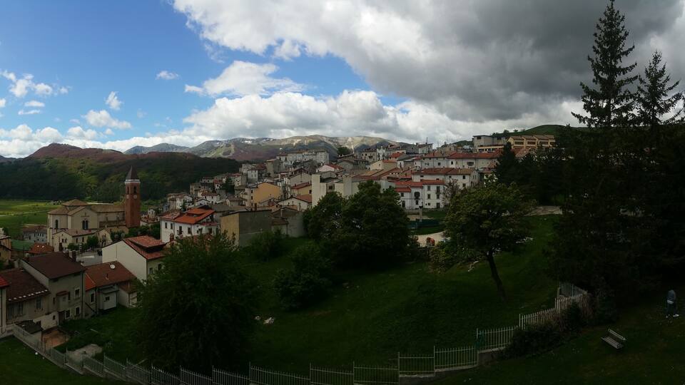 A town nestled in a valley with a prominent church tower, surrounded by lush greenery and mountains in the background.