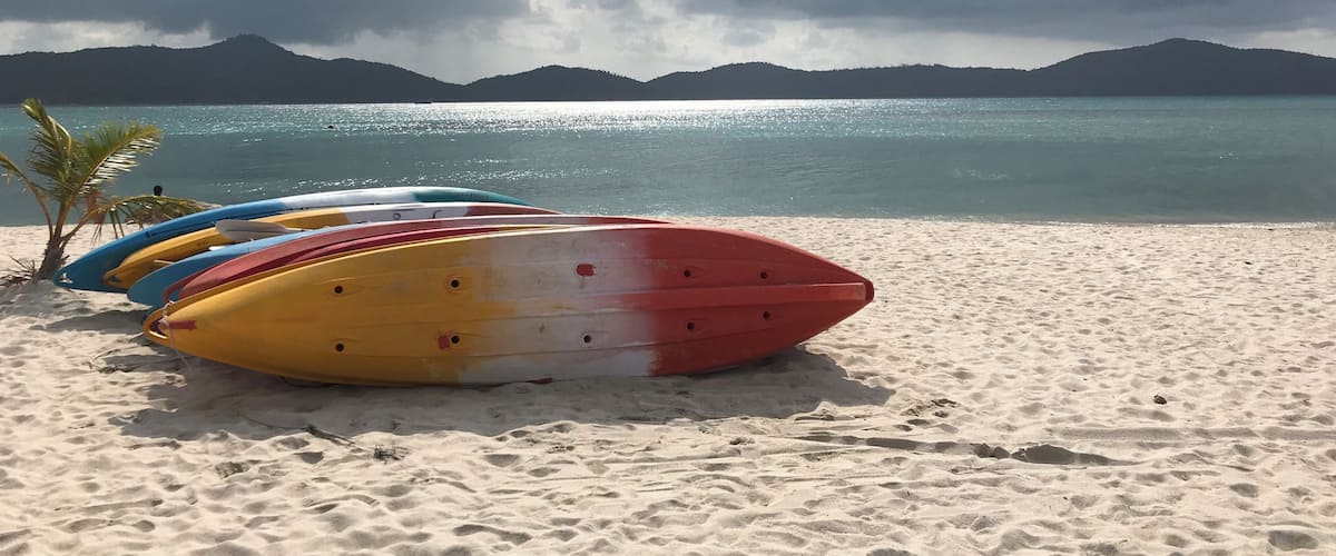 A beach with colorful kayaks lined up and a mountain range in the background.