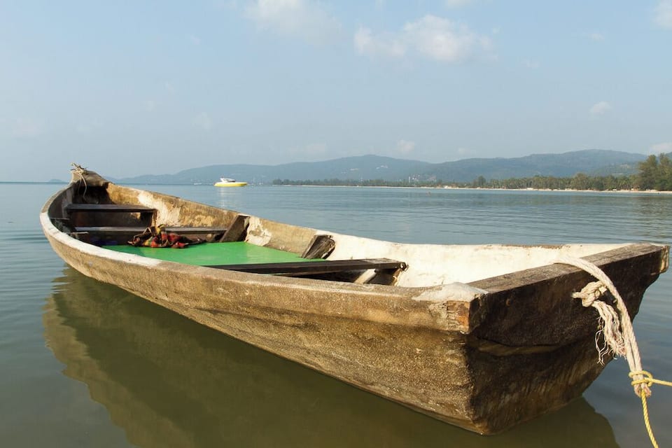 A wooden boat with a green interior floating on calm water, tied to a dock.