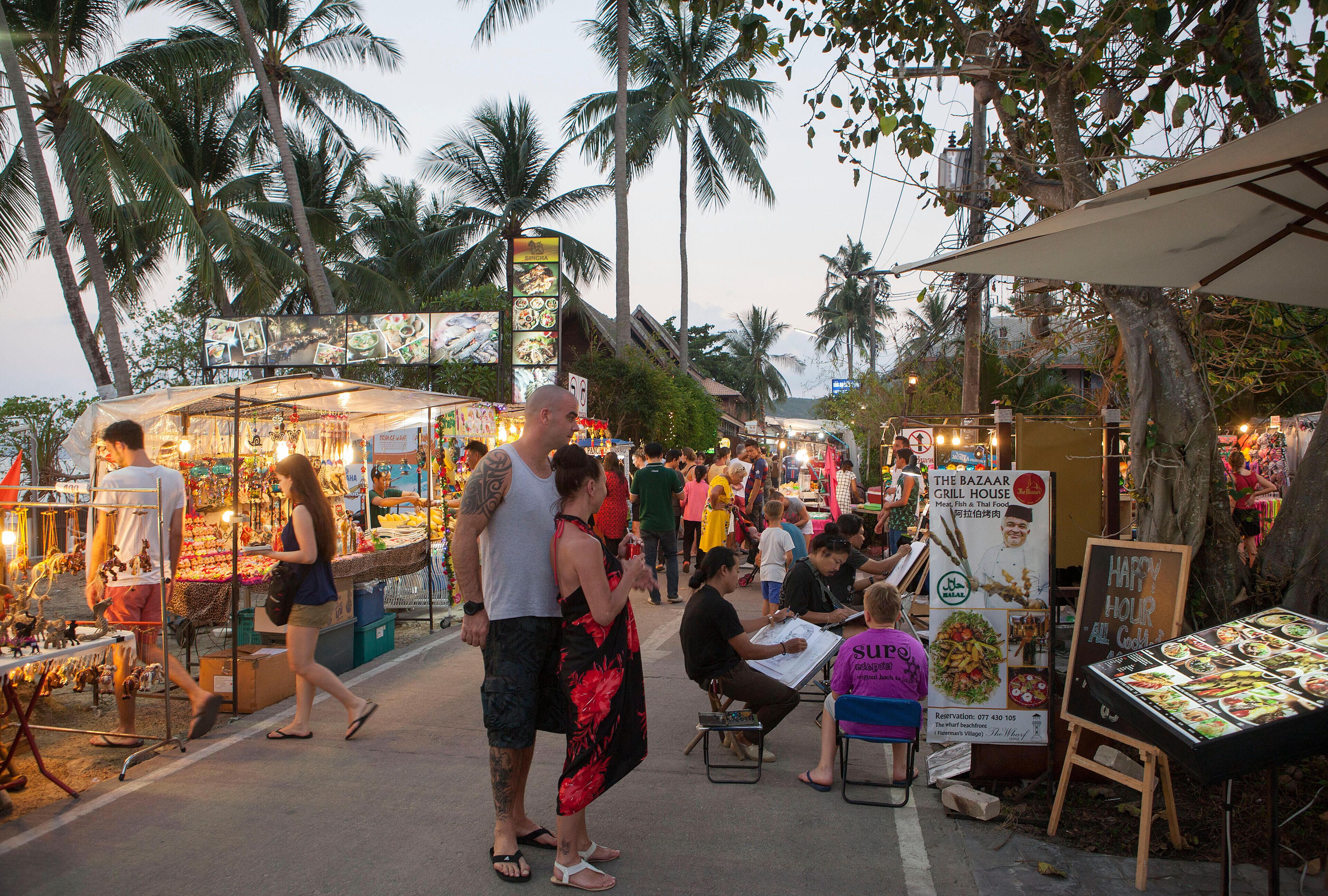 Un mercado callejero animado con puestos que venden comida y artesanías, rodeado de palmeras.