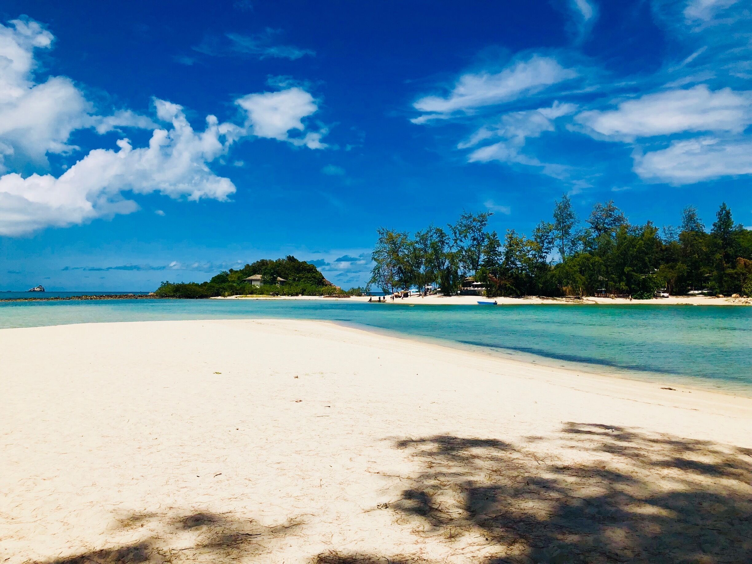 A beach with clear turquoise water, white sand, and a forested island in the background.