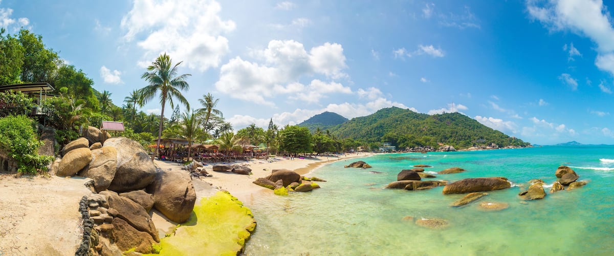 Une plage tropicale aux eaux turquoise et limpides, bordée de grands rochers et d’une végétation luxuriante.