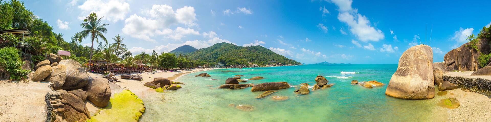Une plage tropicale aux eaux turquoise et limpides, bordée de grands rochers et d’une végétation luxuriante.