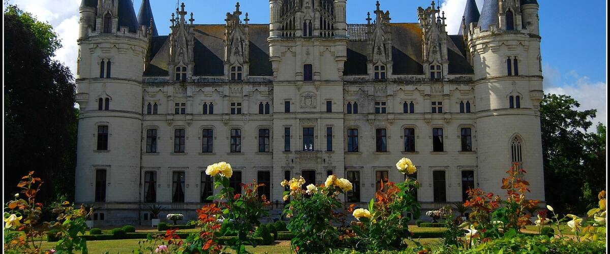 A grand castle with multiple towers and spires, surrounded by a well-maintained garden with various flowers.