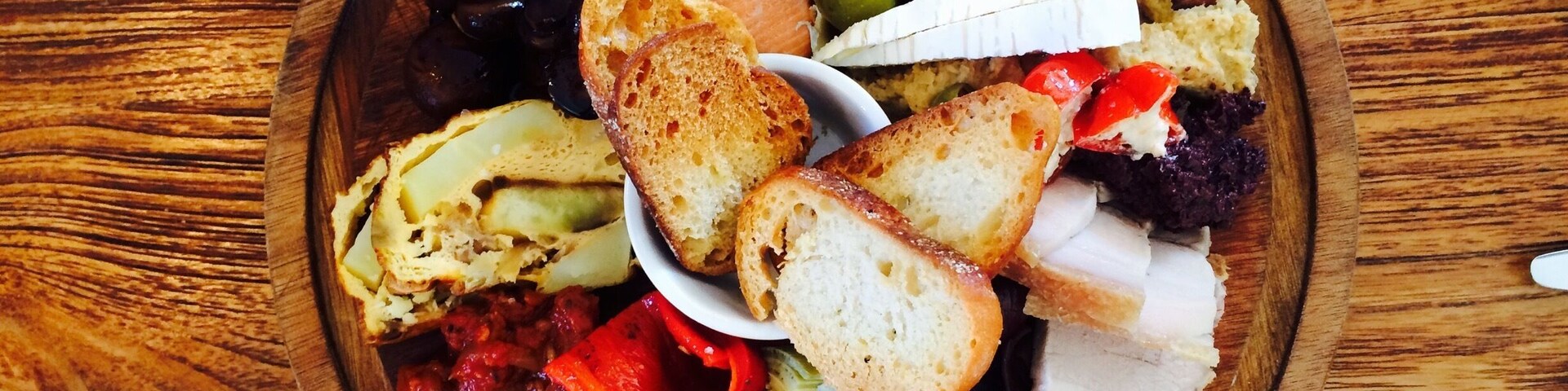 Una bandeja de madera con diversos alimentos, incluyendo salmón, pan y verduras.