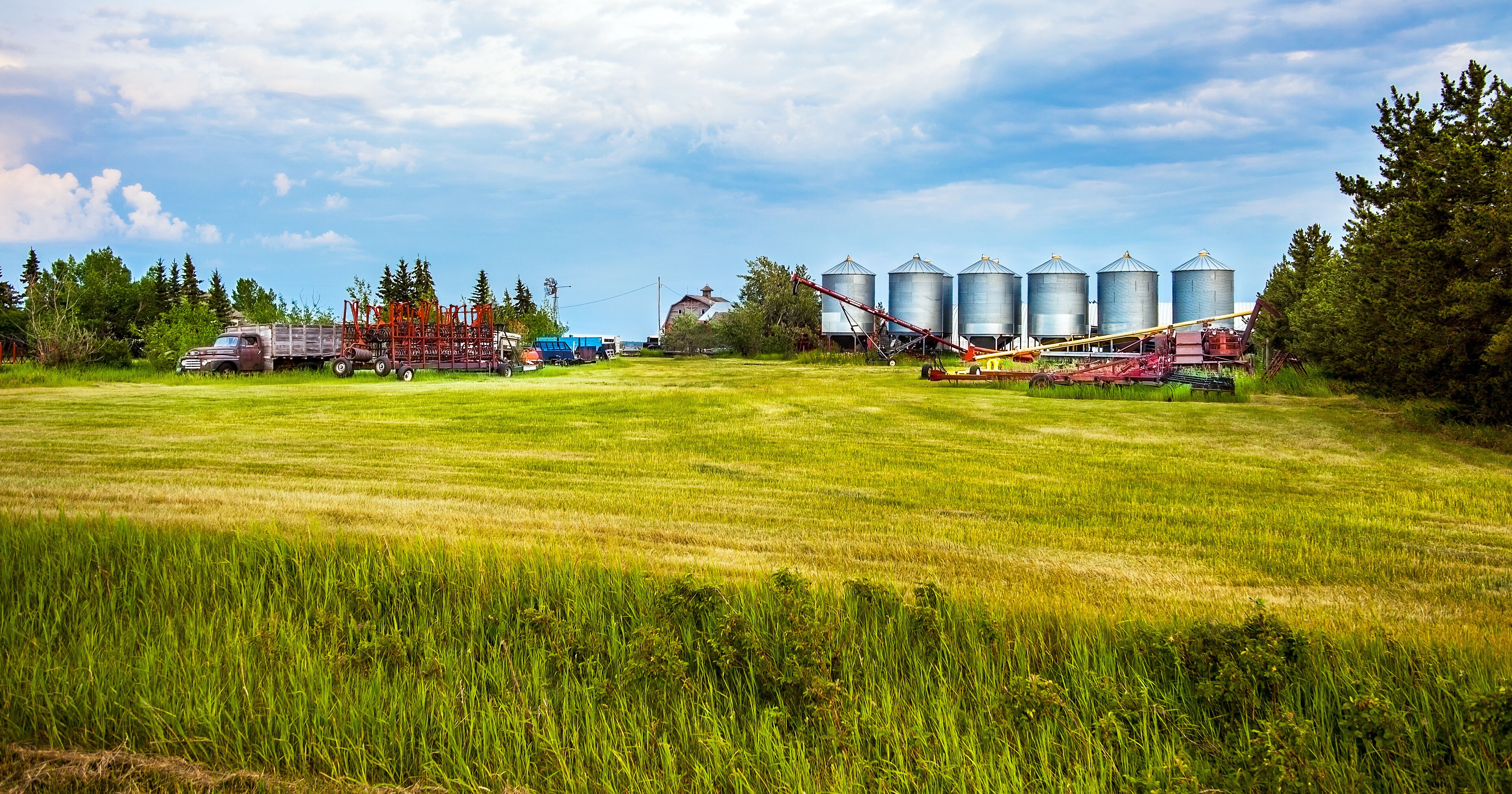 A rural landscape with a field, silos, and agricultural machinery.