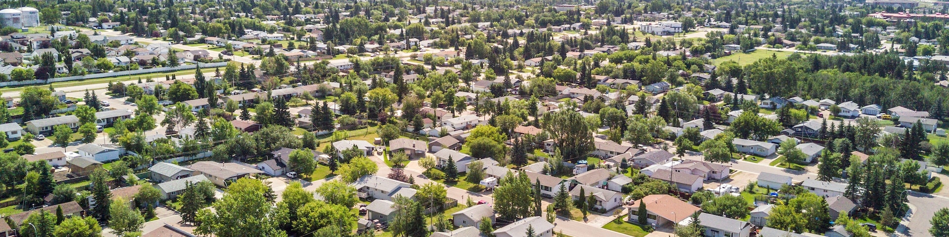 Vista aérea de un barrio residencial con casas, áreas verdes y un paisaje urbano distante.