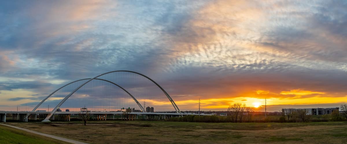A large arched bridge over a river with a sunset in the background.